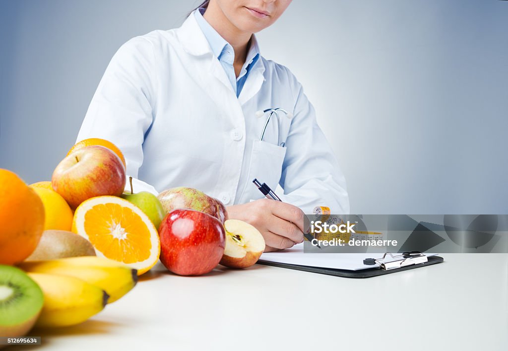 Professional nutritionist writing medical records Professional nutritionist working at desk and writing medical records with fresh fruit on foreground Nutritionist Stock Photo
