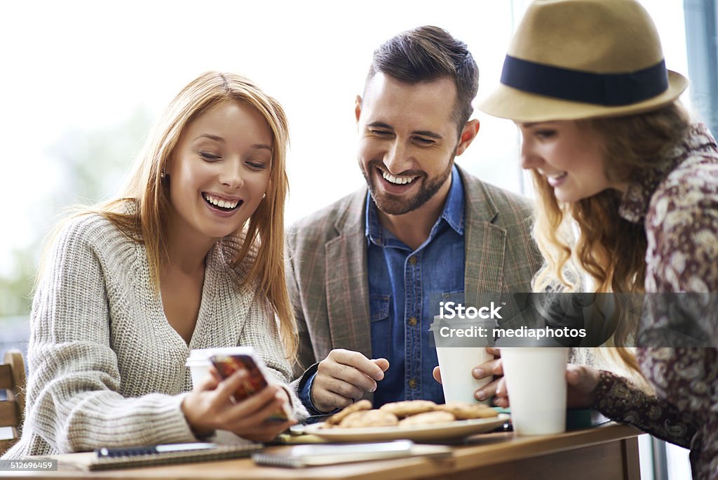 Showing funny pictures Three joyful friends looking at photos on smart phone 20-29 Years Stock Photo