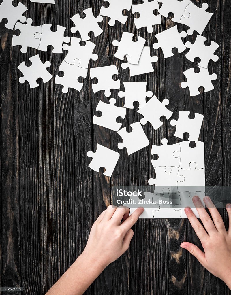 hands starting to collect puzzle pieces hands starting to collect puzzle pieces on dark wooden table Creativity Stock Photo