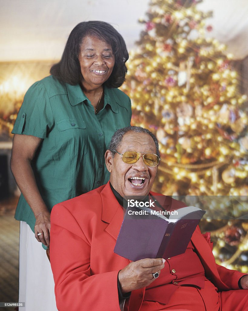 Christmas Bible Read A senior adult man reading scripture in a Christmas-decorated living room.  His wife stands behind looking over his shoulder. Active Seniors Stock Photo