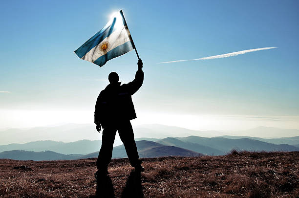 successfull silhouette man winner waving Argentinian flag on top of the mountain peak