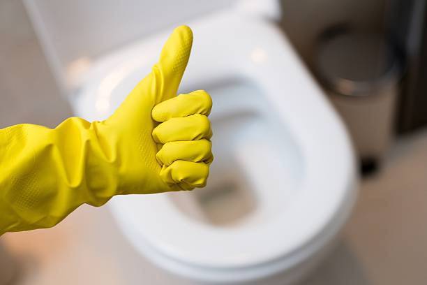 hand with glove showing thumb up sign against clean toilet Close up of female hand with yellow protective rubber glove showing thumb up ok sign against clean toilet. Spring cleaning toilet stock pictures, royalty-free photos & images