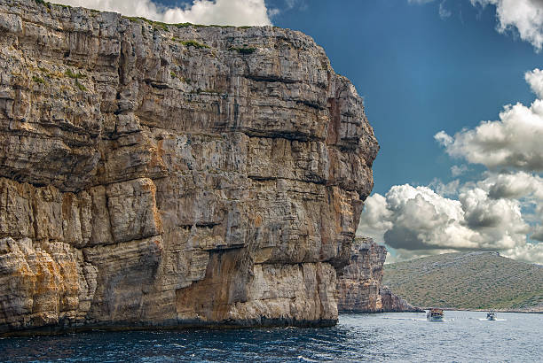 Boats passing huge cliffs of Kornati National Park in Croatia stock photo