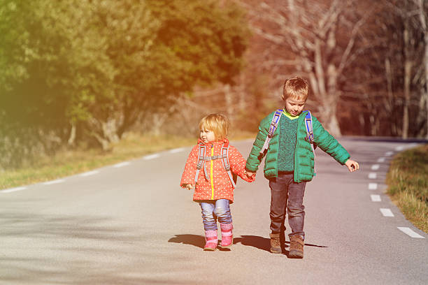 istock brother and sister with backpacks walking on the road 512703362