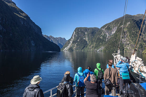 Tourists Group on a Cruise at Doubtful Sound, New Zealand Te Anau, New Zealand - February 6, 2013: DSLR picture of Doubtful Sound in New Zealand. The tourists are looking at the mountains and landscape in the background. The sky is clear blue without any cloud. fiordland national park photos stock pictures, royalty-free photos & images