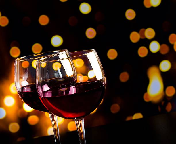 red wine glasses on wood table against bokeh lights background