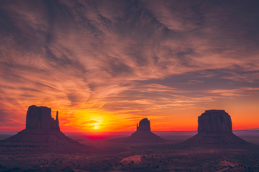 The sun rises between the West and East Mittens in Monument Valley on the border of Arizona and Utah.