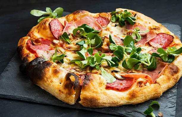 Pizza salami and ham with cheese and cornsalad leaves , rustich fresh baked italian pizza