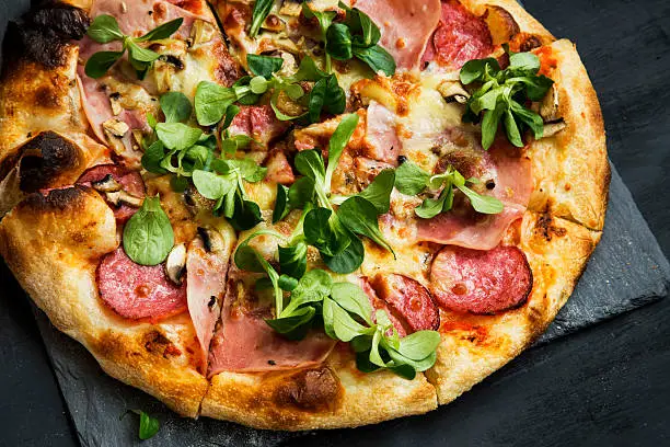 Pizza salami and ham with cheese and cornsalad leaves , rustich fresh baked italian pizza