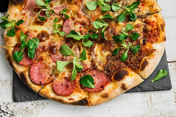 Pizza salami and ham with cheese and cornsalad leaves , rustic fresh baked italian pizza