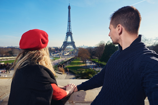 couple holding hands and admirinf Eiffel tower together, feeling tranquil and looking at great view.