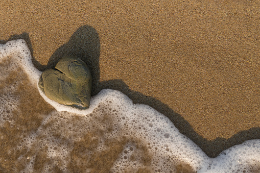 Heart shaped rock washed by the sea on a sandy beach.