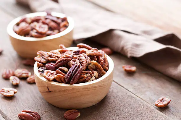 Pecan nuts in wooden bowel on wooden background with copy space for text