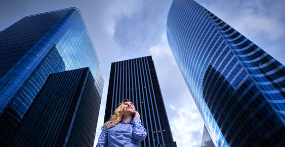 low angle view of business woman with office building behind her talking on the phone and expressing positivity.