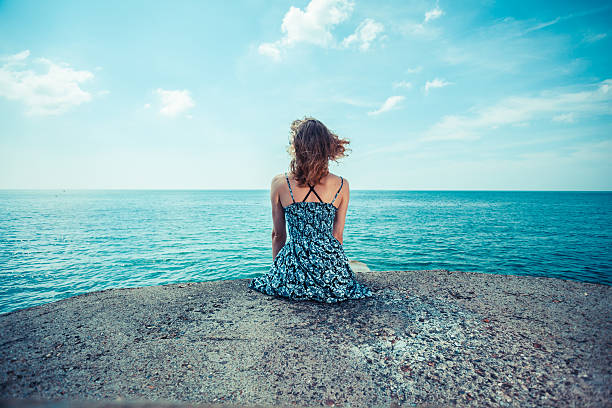 istock Young woman sitting by the ocean 512750227