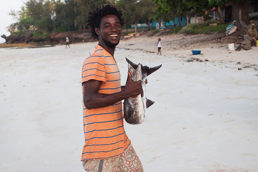 Zanzibar. Tanzania - December 23, 2015: Young black fisherman with big fish on the beach smiling. Kizimkazii. Zanzibar