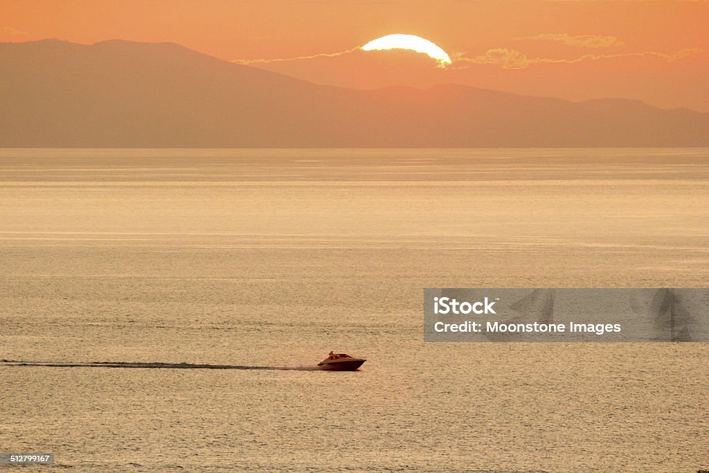 Mykonos in the Cyclades, Greece A speedboat motors past the setting sun in Mykonos Activity Stock Photo