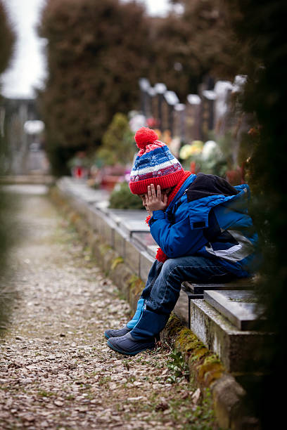 istock Sad little boy, sitting on a grave in a cemetery 512799902