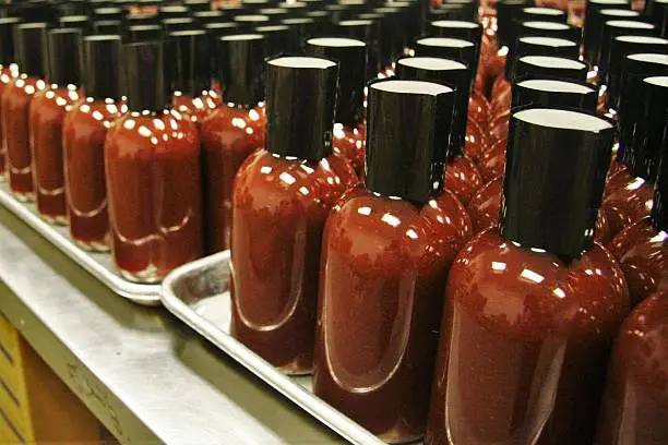 A row of unlabeled cylindrical bottles of hot sauce on a silver tray, with black caps.