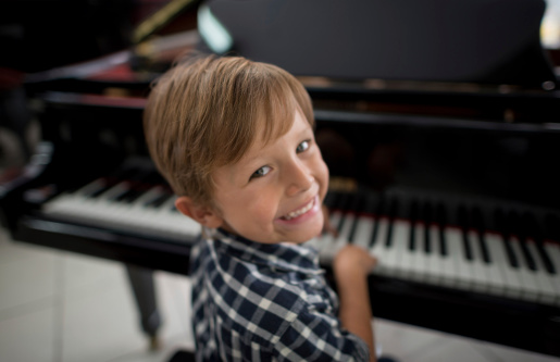 Portrait of five years old kid practicing music instrument at home. Happy asian little boy smiling and playing the digital piano.