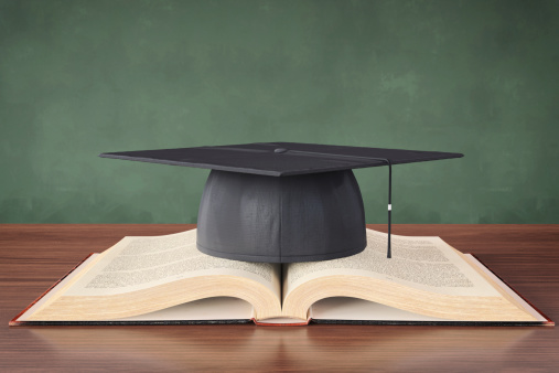 Open book and mortar board in front of chalk board.