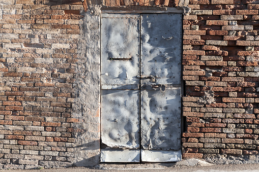 Gray rusted metal door in old brick wall, background photo texture