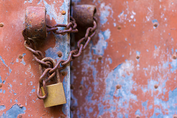 A bronze padlock and rusty old chain on an antique peeling pink tin door (close-up). Shot in Italy.  Copy space available.
