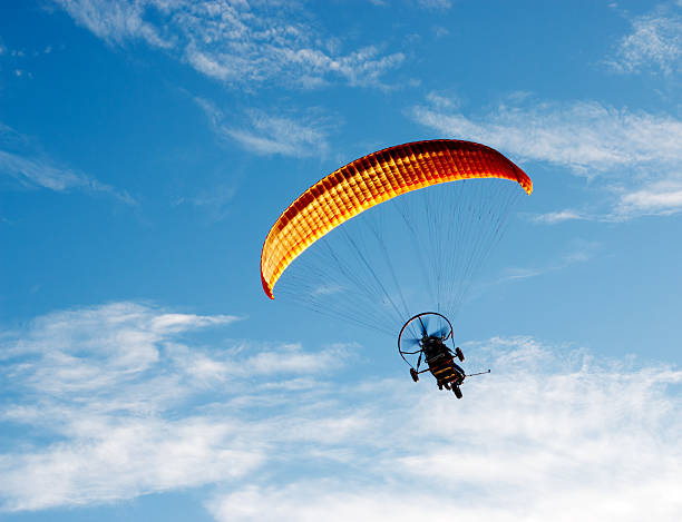 Powered paraglider Unidentified Paraglider with motor flies on a blue sky background. Man paragliding with a motorized parachute. para ascending stock pictures, royalty-free photos & images