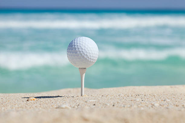 Golf ball and tee on beach with ocean waves behind stock photo