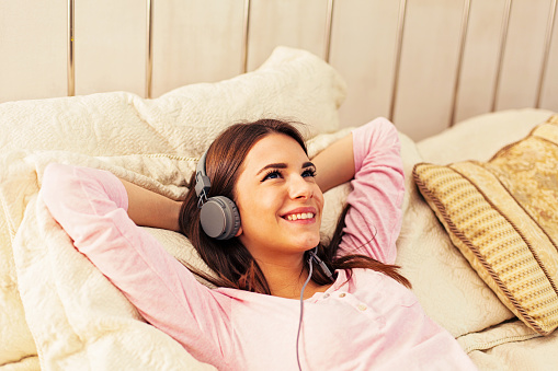 Young girl listening to music, wearing headphones lying down on the bed