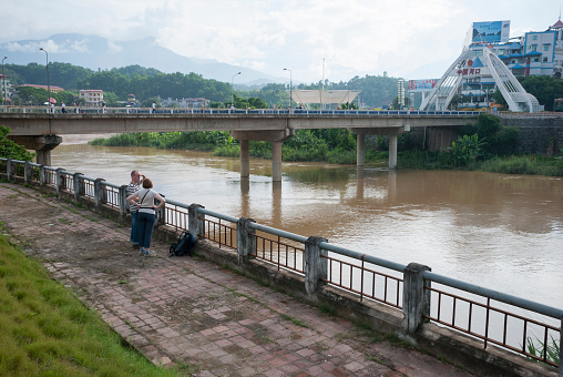 Lao Cai, Vietnam - July 29, 2007: Two tourists stand on an embankment above the Red River in Lao Cai, Vietnam. The bridge is a border crossing connecting the town to Hekou, China