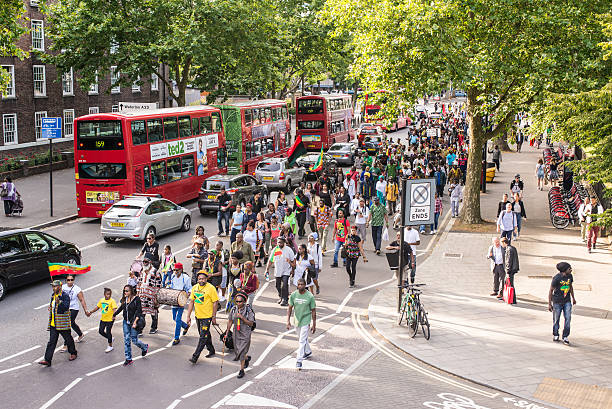 Street demonstration with people marching in a busy road London, UK - August 1, 2015: Street demonstration with Afro-caribbean people marching in a busy road in London, with flags and drums. brixton stock pictures, royalty-free photos & images