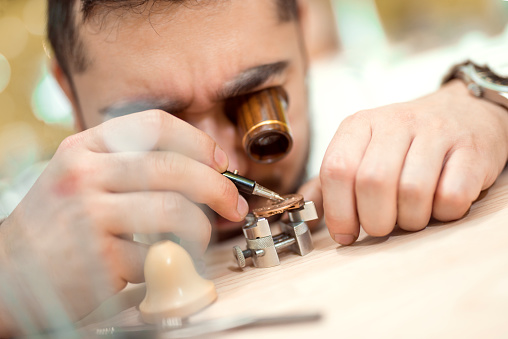 Close up  portrait of a watchmaker at work. He is wearing specialist magnifying glass.Old pocket watch being repaired by watch maker.