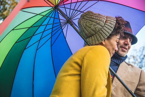 Couple in a park, under colorful umbrella. They are smiling and having fun.