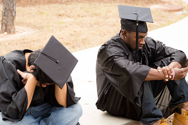 Female graduate looking through binoculars against cloudy sky.