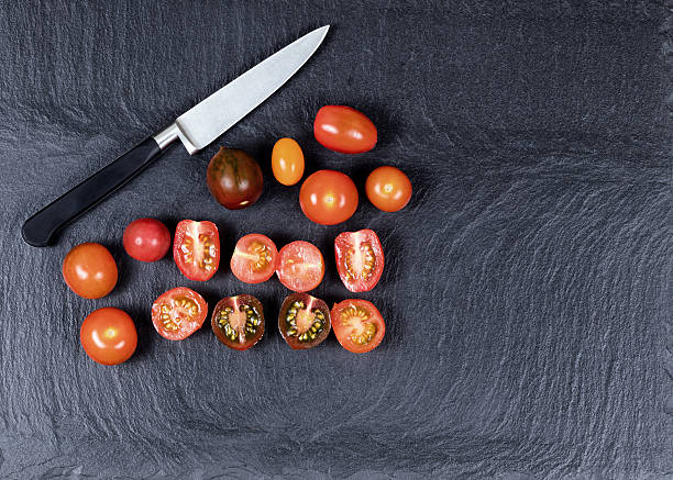 istock Colorful mixed small tomatoes and cutting knife on natural black 512824838