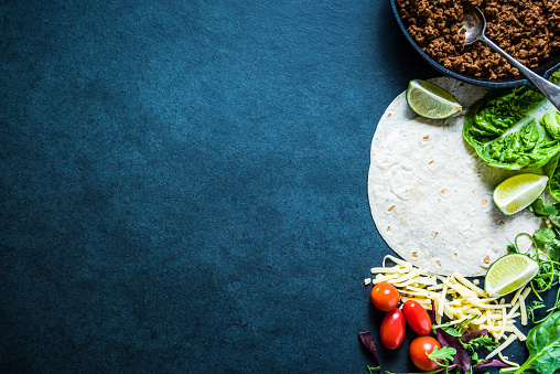 Mexican fajitas or tortillas, food border background with space for text or recipe. Overhead on dark slate.