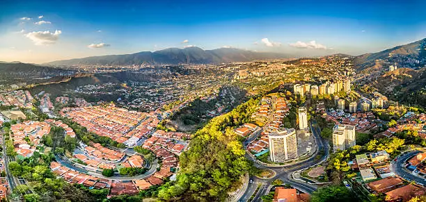 Panoramic image of eastern Caracas city aerial view at late afternoon. Venezuela.  Showing El Avila mountain also known as El Avila National Park (Guaraira Repano).  Santiago de Leon de Caracas, is the capital city of Venezuela and center of the Greater Caracas Area. It is located in the northern part of the country, following the contours of the narrow Caracas Valley and the "Cordillera de la Costa". The valley is close to the Caribbean Sea, separated from the coast by a steep 2,200 m (7,200 ft) high mountain range, Cerro El Avila. To the south there are many more hills and mountains with residential constructions. Caracas is divided into five municipalities: Libertador, Chacao, Baruta, Sucre, and El Hatillo. Libertador holds many of the government buildings and is the Capital District (Distrito Capital). The Metropolitan Region of Caracas has an estimated population of 5,250.000.