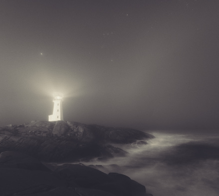 A fogbank begins to thin, revealing the stars above Peggy's Cove Lighthouse.  Long exposure in heavy surf, toned black and white.