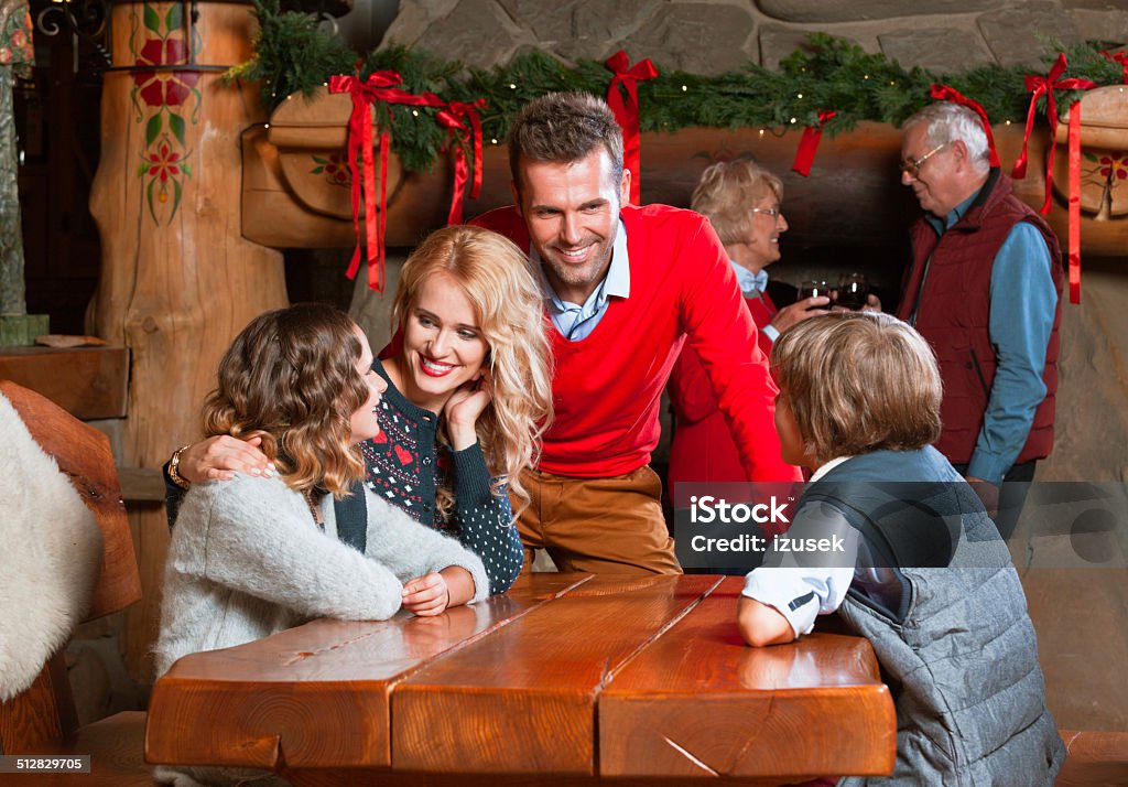 Christmas Time Happy parents talking with their children at the table at home with granparents standing by the fireplace in the background.  Christmas Stock Photo