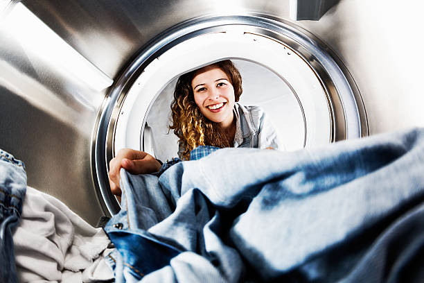 Smiling blonde beauty loads her tumble dryer: seens from inside In an unusual view from inside the washing machine drum, a smiling and pretty blonde loads - or unloads - laundry. washing machine photos stock pictures, royalty-free photos & images