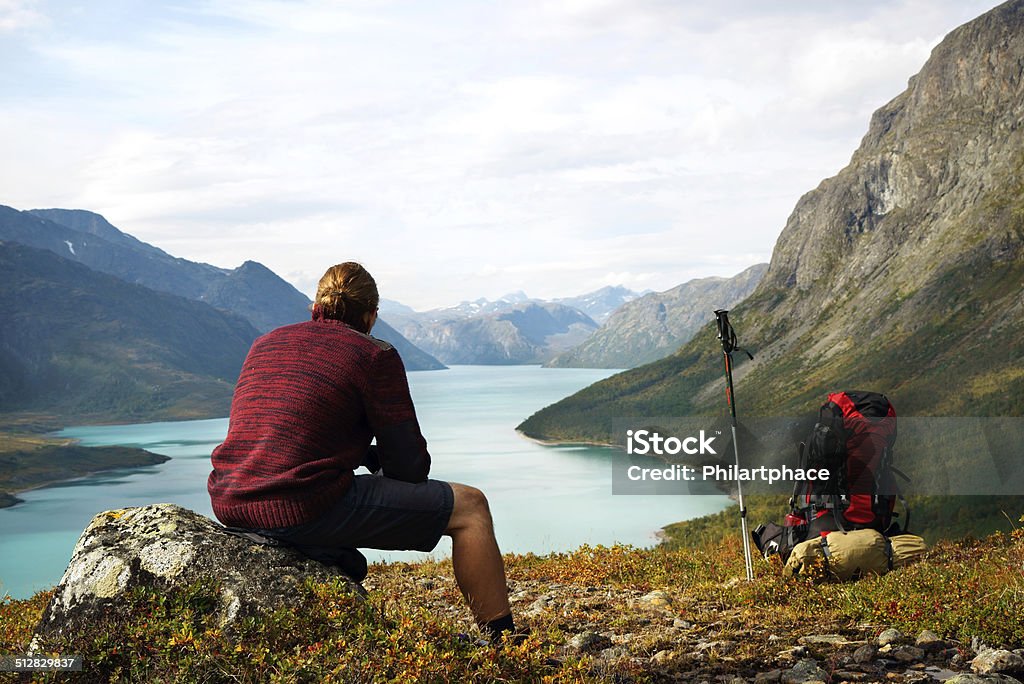 Scenic view of lake Gjende in the Jotunheimen national park Hiking young man is sitting in front of a picturesque scenic view of Gjendesee and a remote mountain range in the Jotunheimen national park, Norway. XXXL (Sony Alpha 7R) Adult Stock Photo