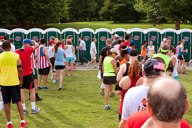 10K Runners Wait In Line To Use Portable Toilets Atlanta, GA, USA - July 4, 2014:  Exhausted runners wait in long lines to use a Johnny On The Spot portable toilet, after just completing the Peachtree Road Race 10K. portable toilet stock pictures, royalty-free photos & images