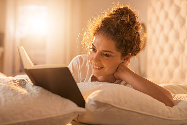 istock Happy woman enjoying in a book while relaxing in bed. 512884178