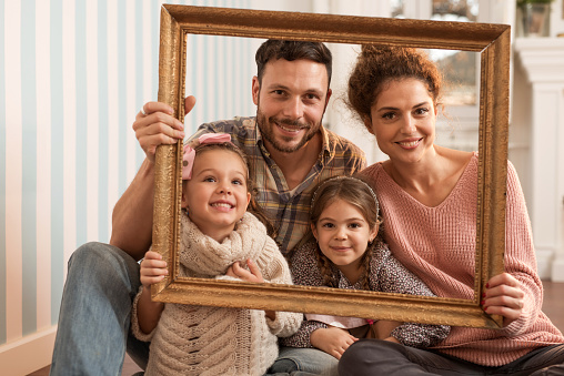 Portrait of young happy family holding a picture frame and looking at the camera.