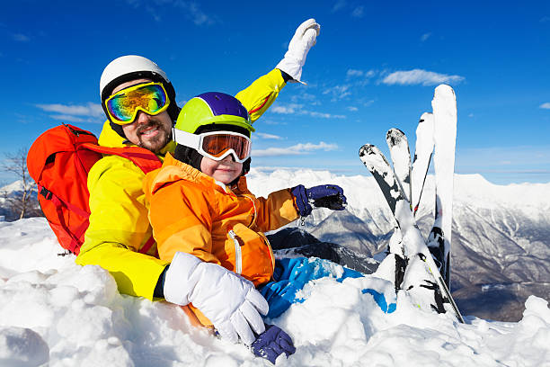 istock Dad and son skiers sit in snow on mountain top 512885864