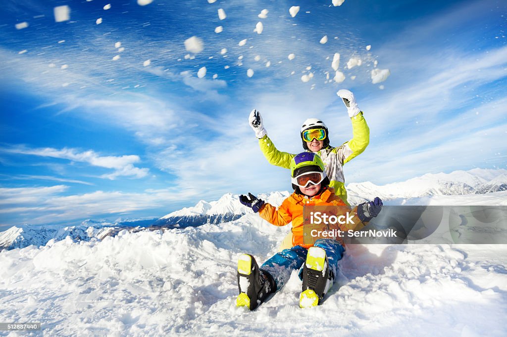 Mother and son on the mountain happy throw snow Mom and child with ski outfit mask and helmet sit and throw up snow Skiing Stock Photo