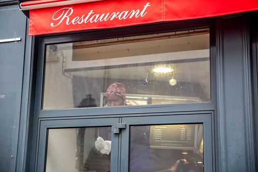 Paris, France - January 5, 2016: Woman cleaning inside of restaurant window of Montmartre restaurant shot from the street outside