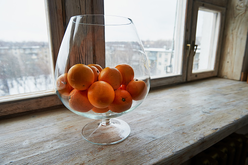 Large glass vase with oranges on wooden windowsill