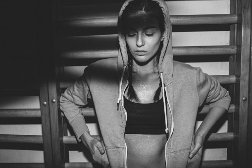 Photo of a young determined woman wearing hoodied sweatshirt after having her evening exercise in the gym.